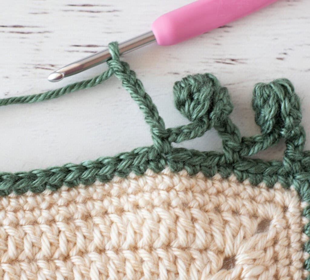 Step by step photo of crochet pom pom border in green yarn on an ivory blanket