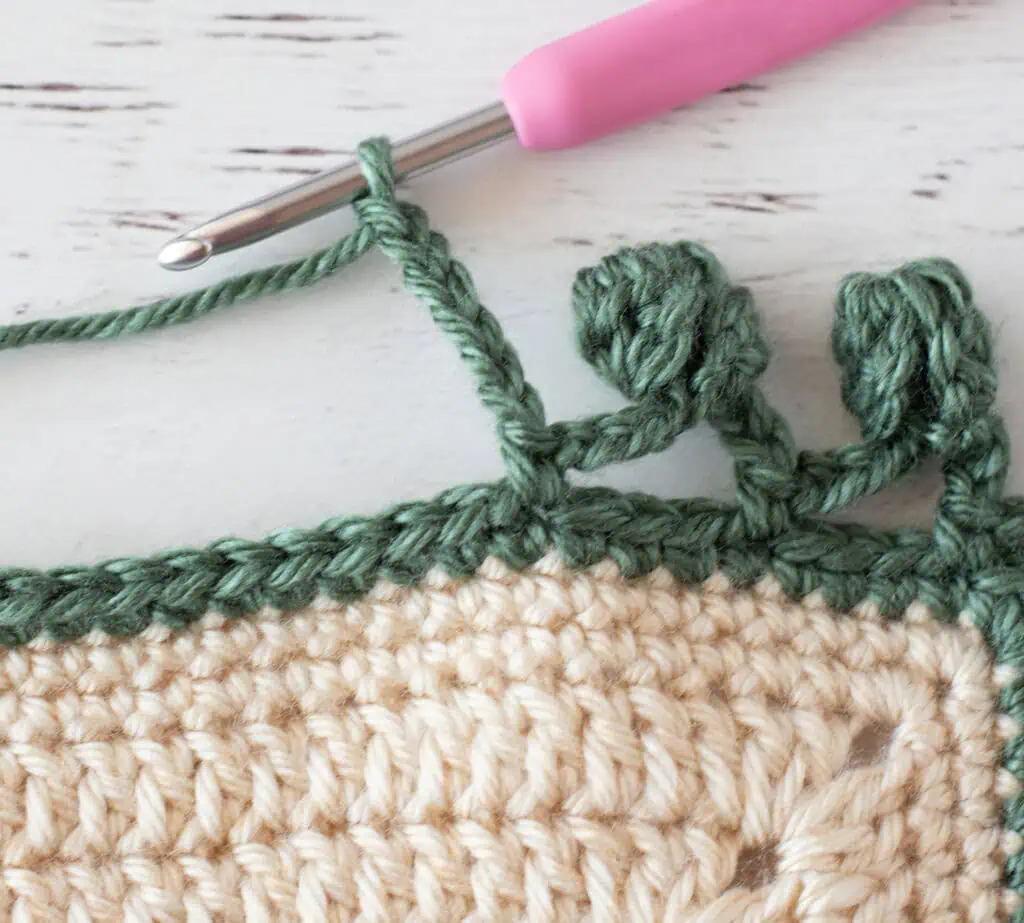 Step by step photo of crochet pom pom border in green yarn on an ivory blanket