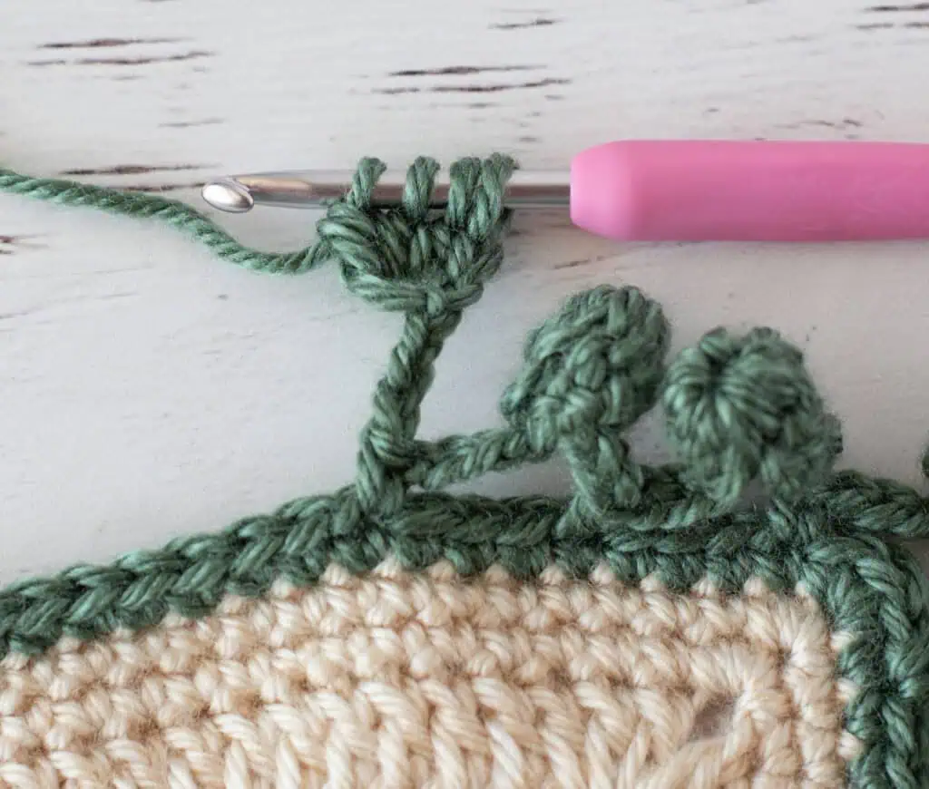 Step by step photo of crochet pom pom border in green yarn on an ivory blanket