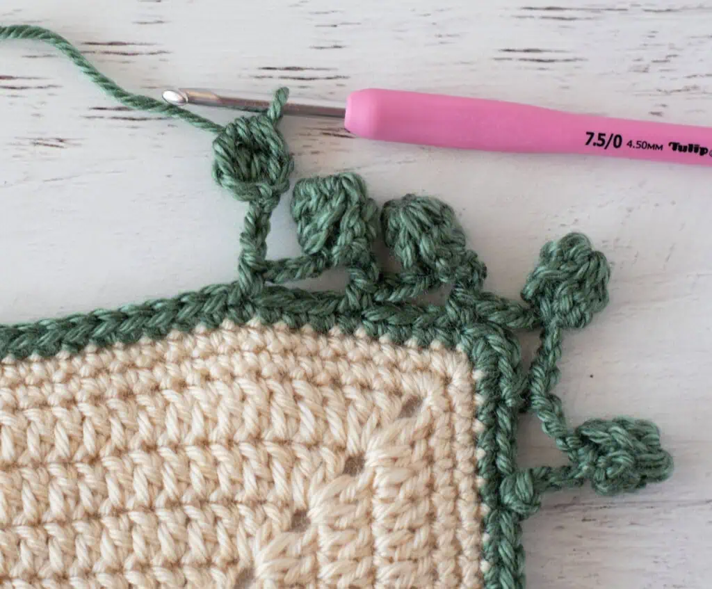 Step by step photo of crochet pom pom border in green yarn on an ivory blanket