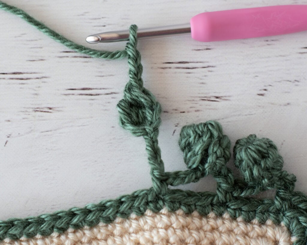Step by step photo of crochet pom pom border in green yarn on an ivory blanket