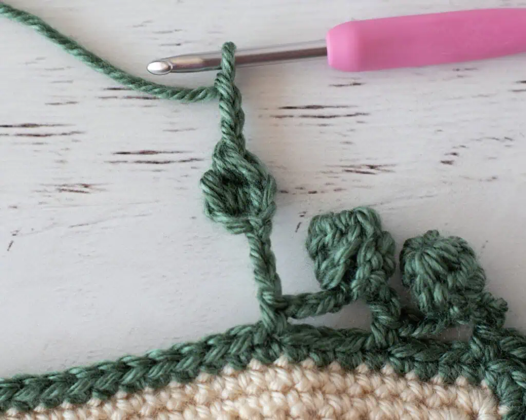 Step by step photo of crochet pom pom border in green yarn on an ivory blanket