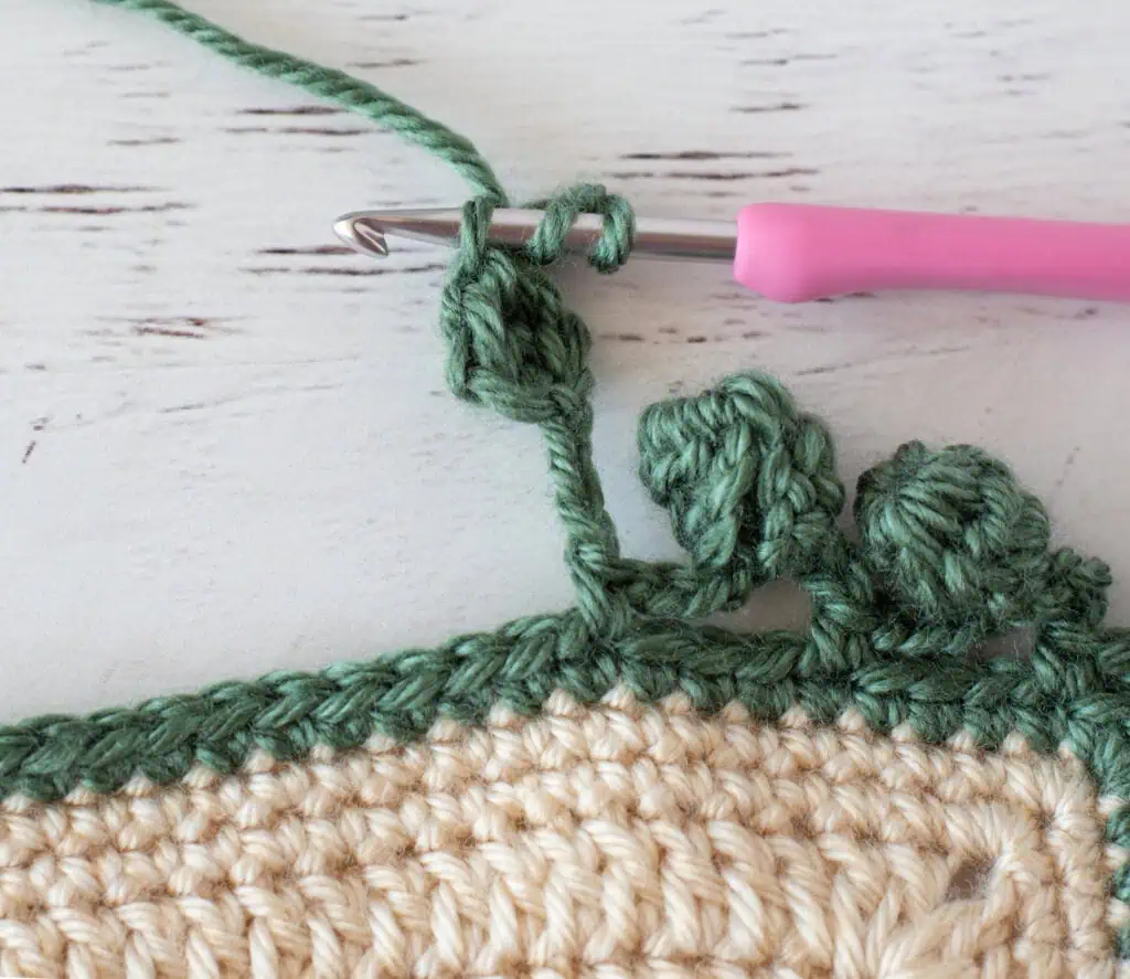 Step by step photo of crochet pom pom border in green yarn on an ivory blanket
