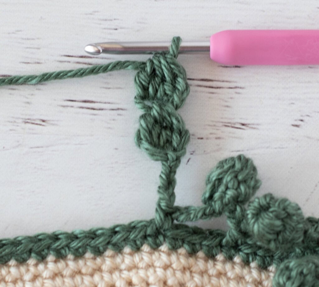 Step by step photo of crochet pom pom border in green yarn on an ivory blanket