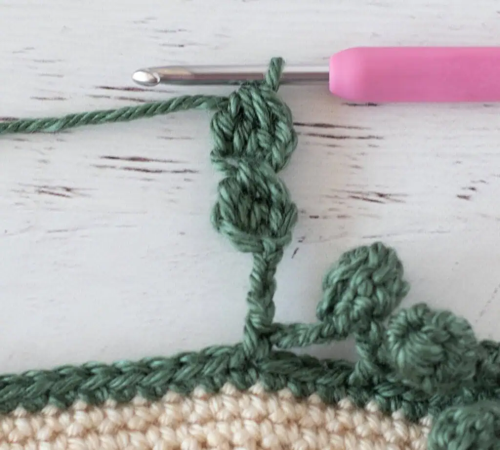 Step by step photo of crochet pom pom border in green yarn on an ivory blanket