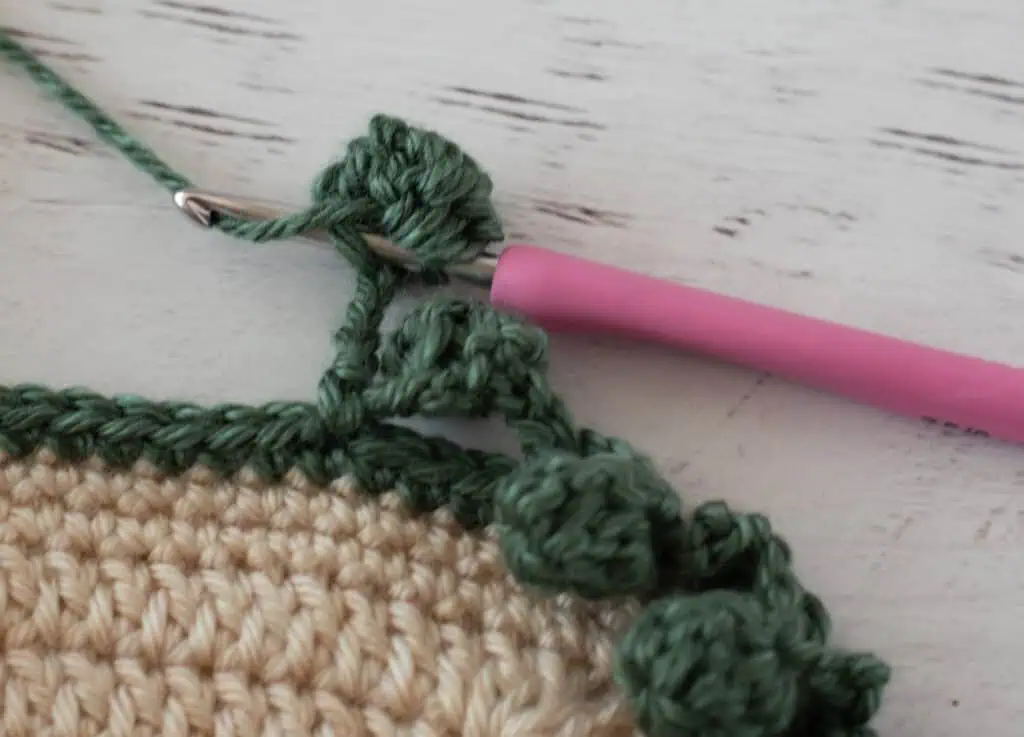 Step by step photo of crochet pom pom border in green yarn on an ivory blanket