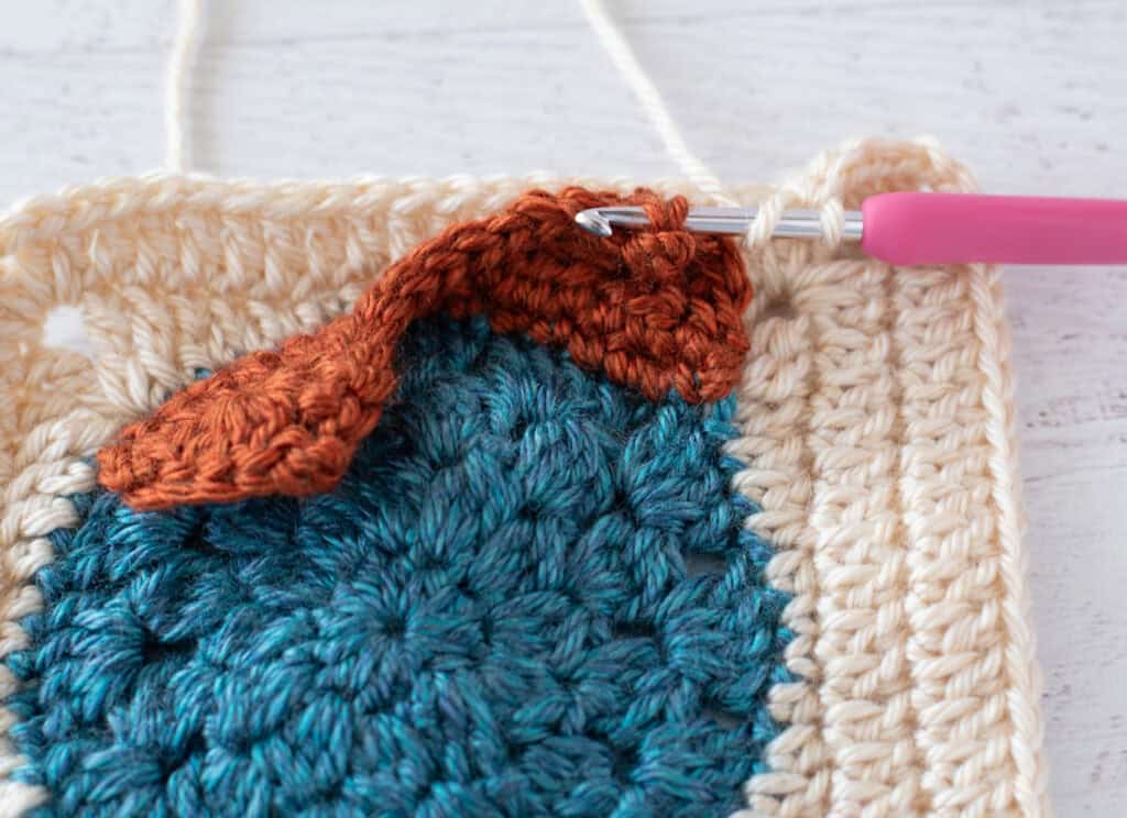 Owl afghan block in progress with blue, orange and cream afghan square and pink hook