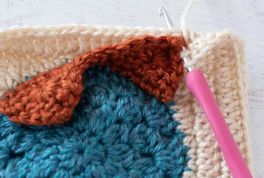 blue, orange and cream crochet granny square with pink hook