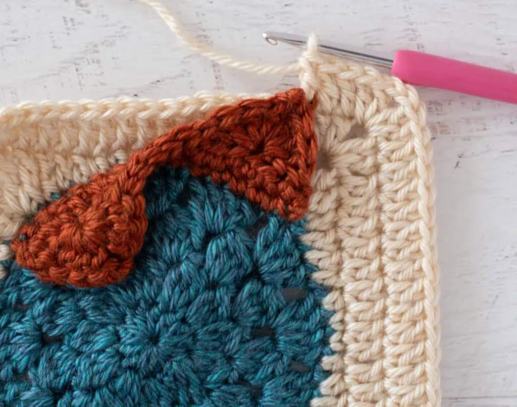 blue, orange and cream crochet granny square with pink hook