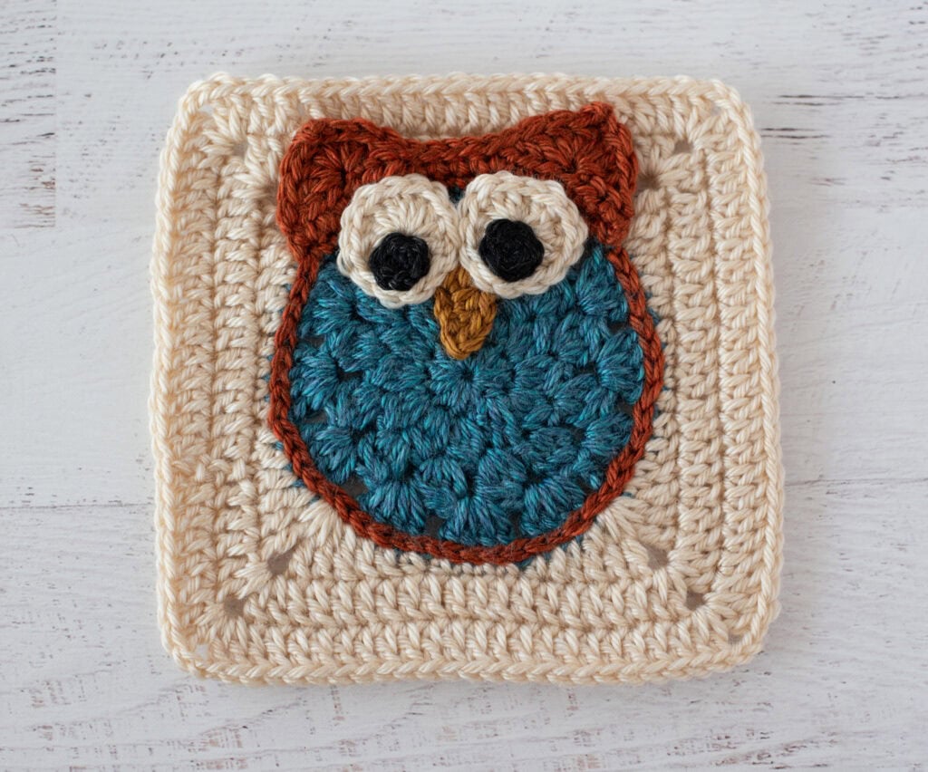 Crochet owl granny square in blue and orange yarn on a cream afghan square
