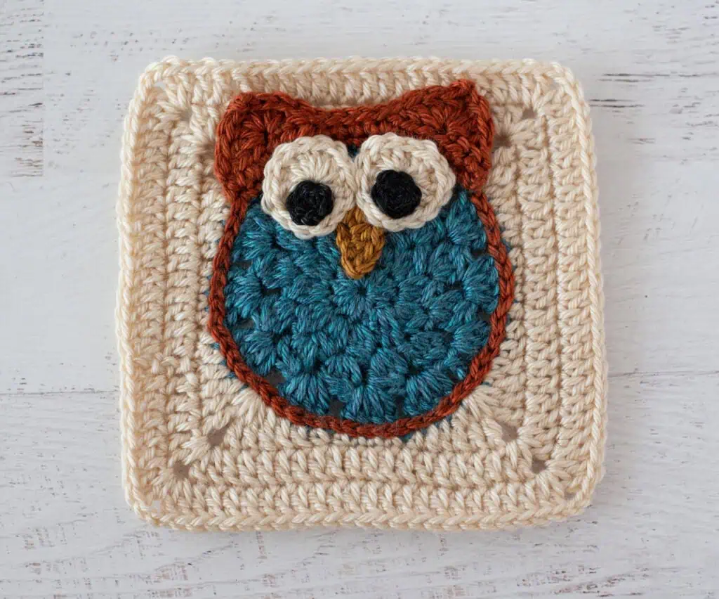 Crochet owl granny square in blue and orange yarn on a cream afghan square