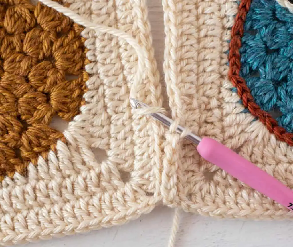 close up view crocheting owl afghan squares together with cream yarn