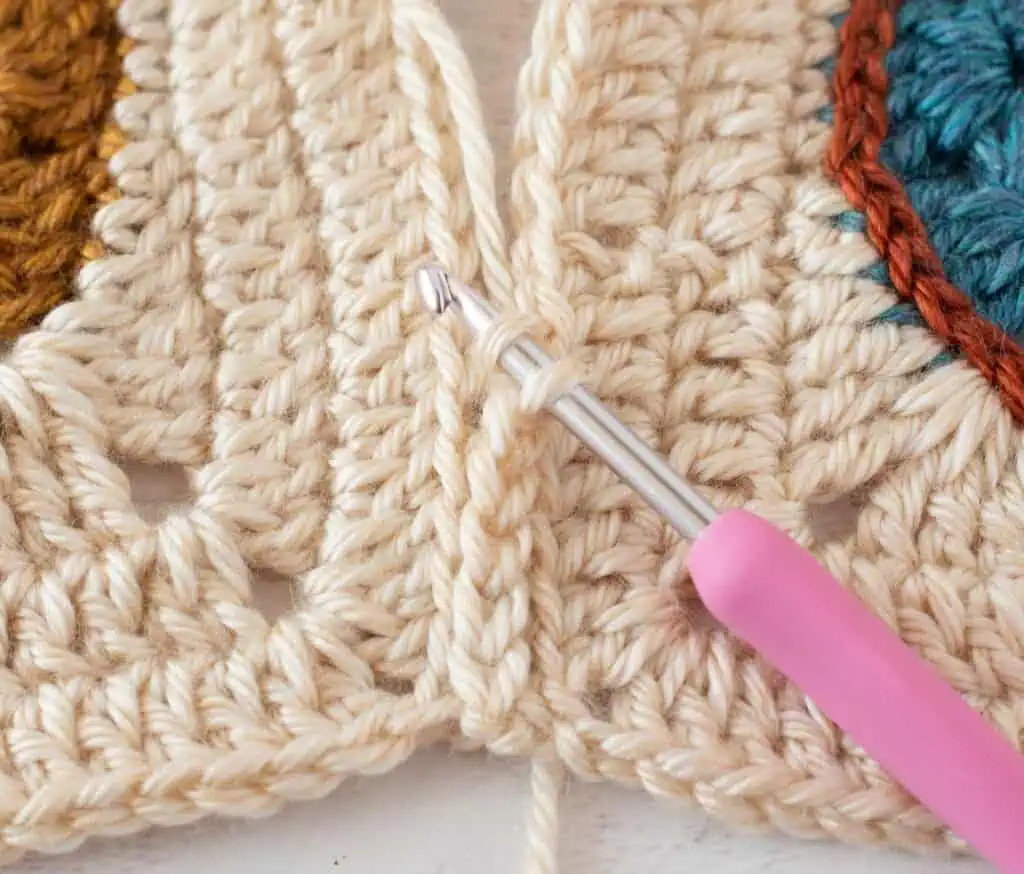 close up view crocheting owl afghan squares together with cream yarn