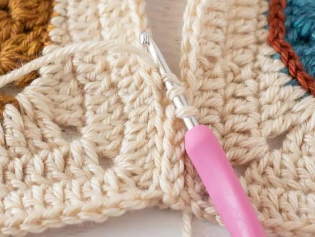 close up view crocheting owl afghan squares together with cream yarn