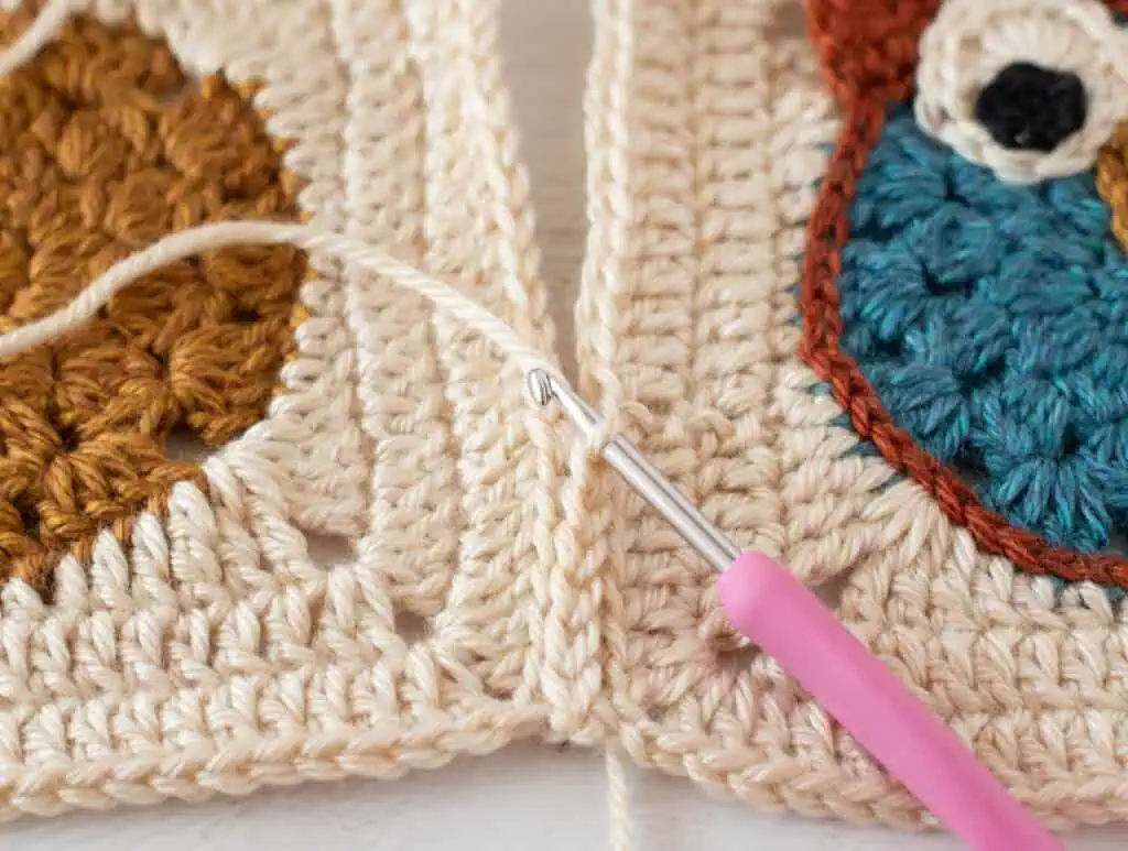 close up view crocheting owl afghan squares together with cream yarn