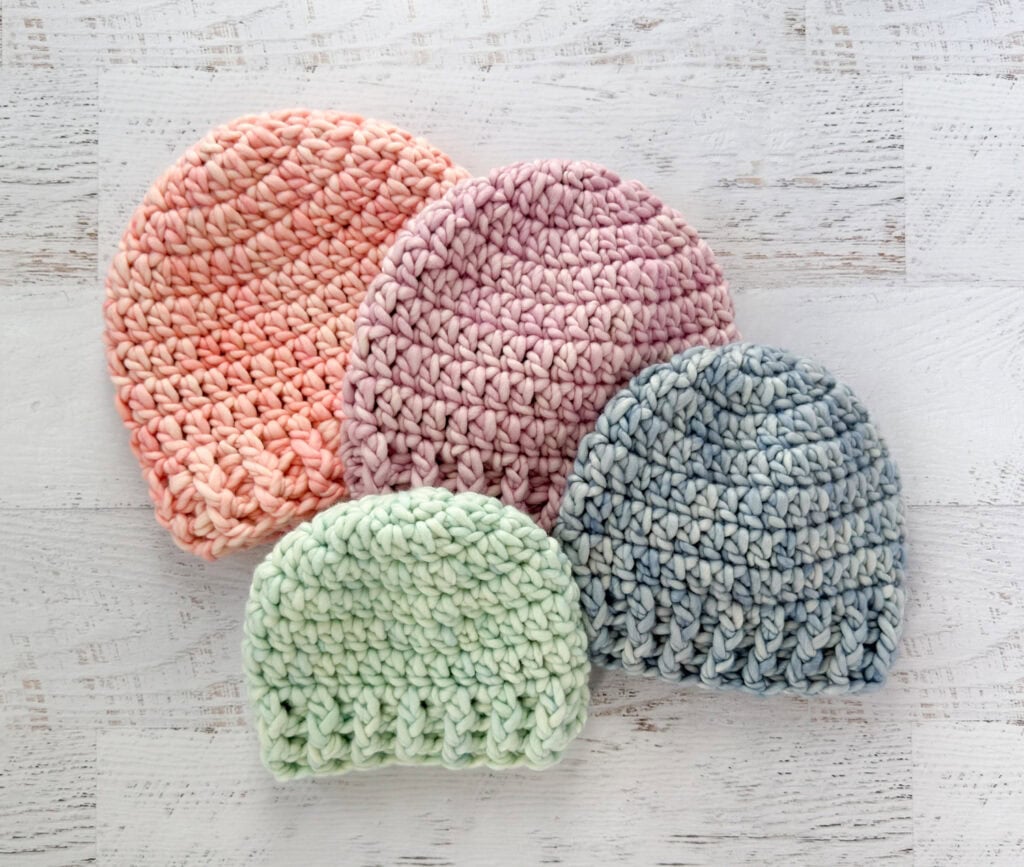 4 crochet hats in pink, purple, blue and green yarn.