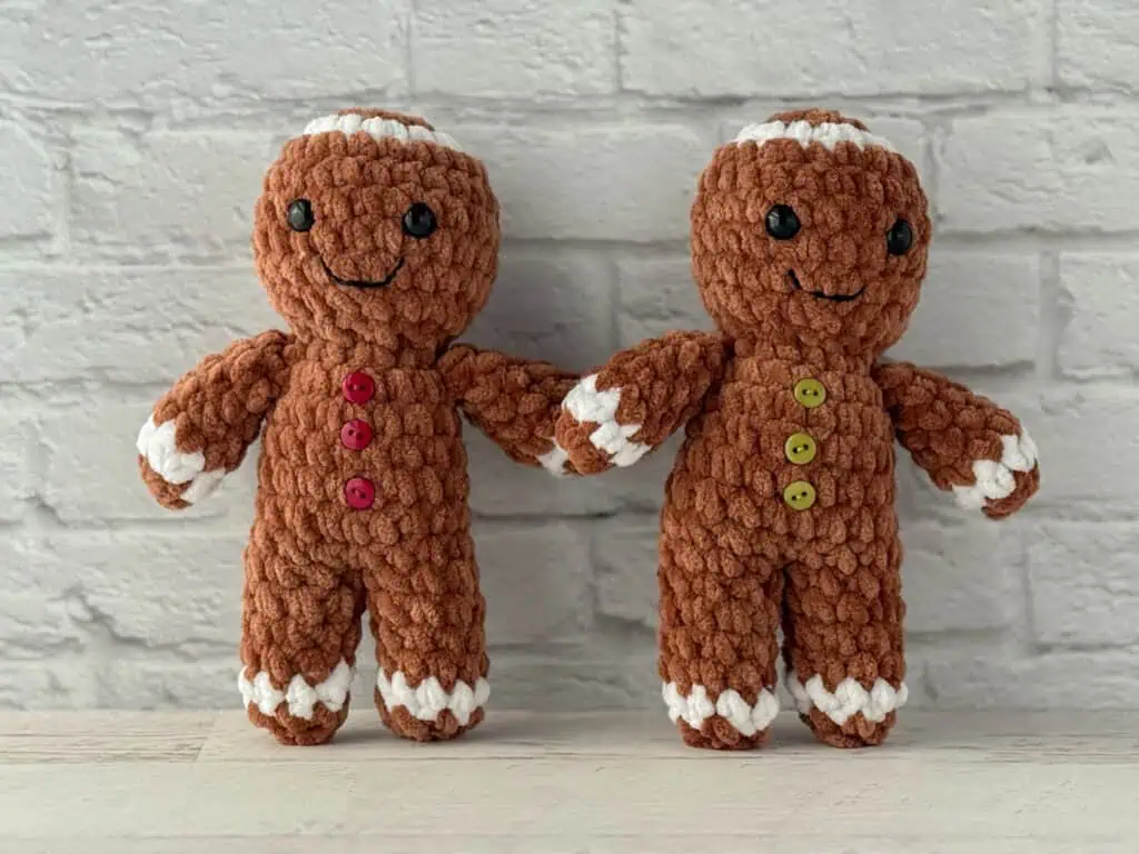Crocheted plush gingerbread standing on a whitewashed table, features brown and white yarn and red buttons.