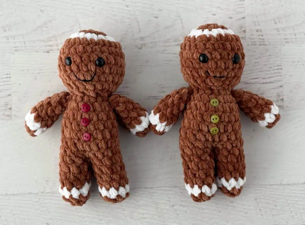 Crocheted plush gingerbread men on a whitewashed table, features brown and white yarn and red and green buttons.