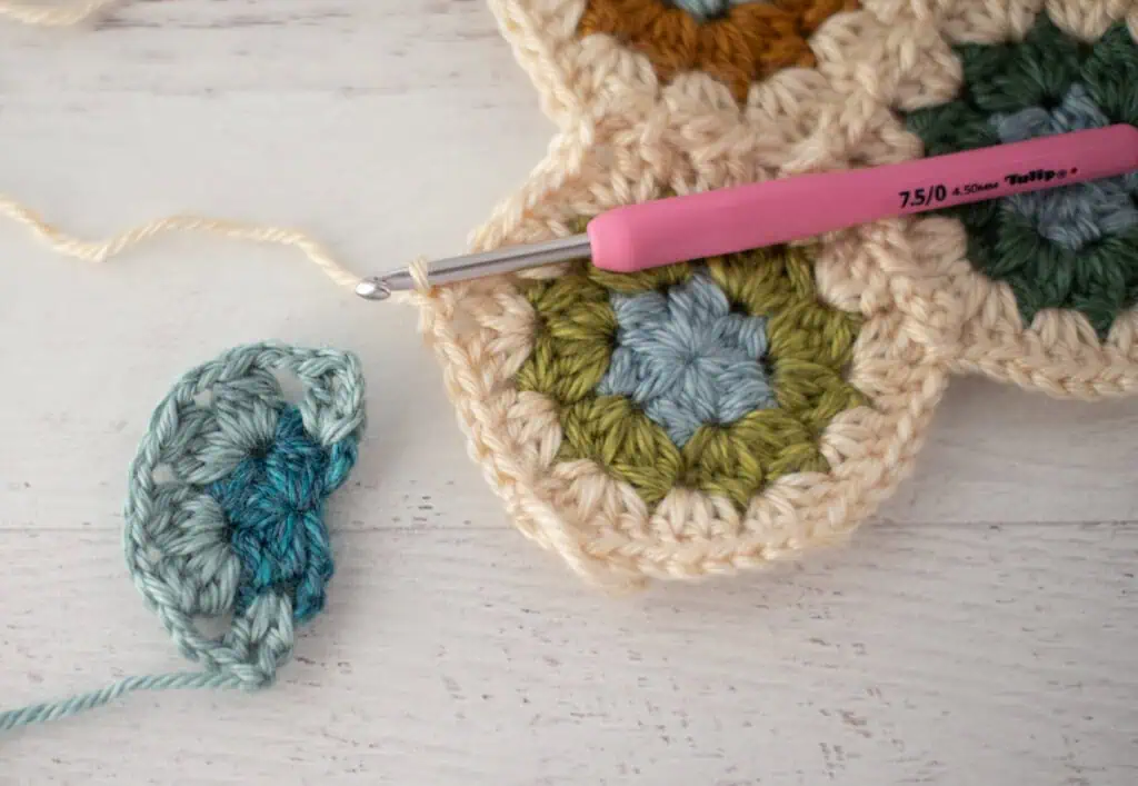 Close-up of crochet granny hexagons made with colorful yarn and a pink crochet hook.