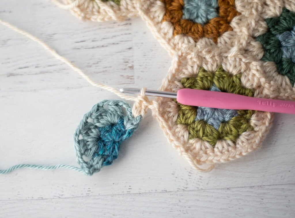 Close-up of crochet granny hexagons made with colorful yarn and a pink crochet hook.
