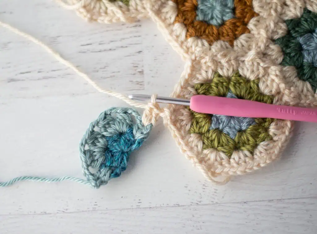 Close-up of crochet granny hexagons made with colorful yarn and a pink crochet hook.