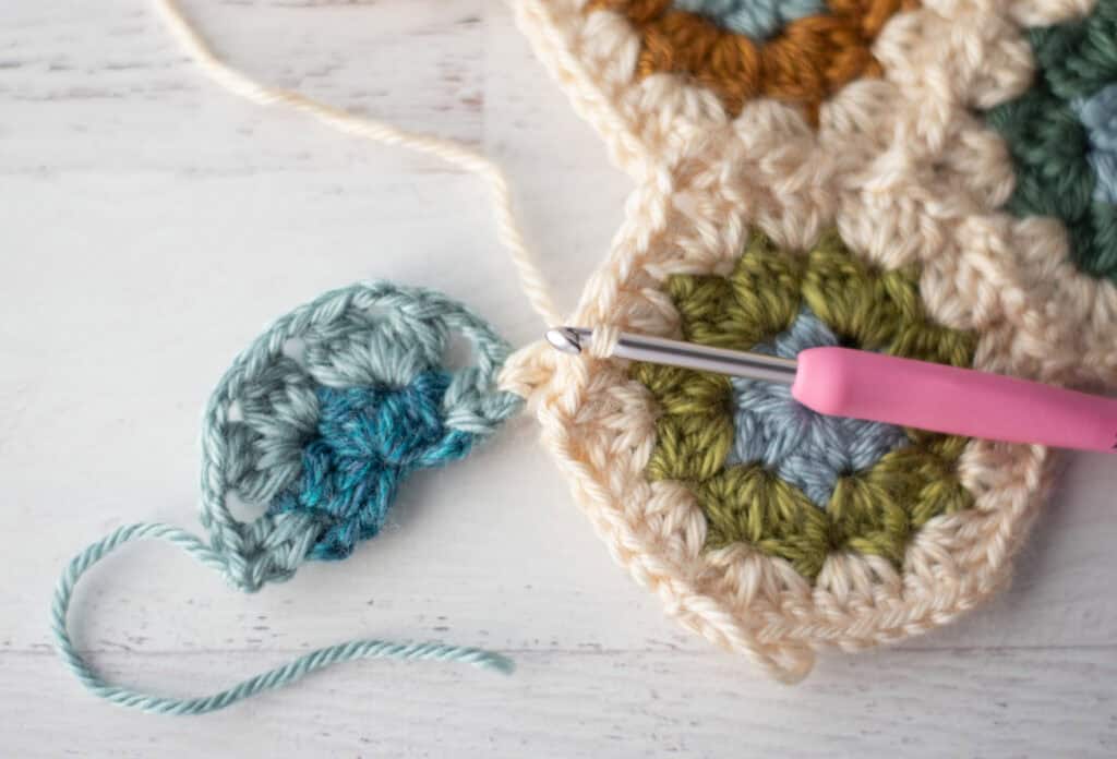 Close-up of crochet granny hexagons made with colorful yarn and a pink crochet hook.