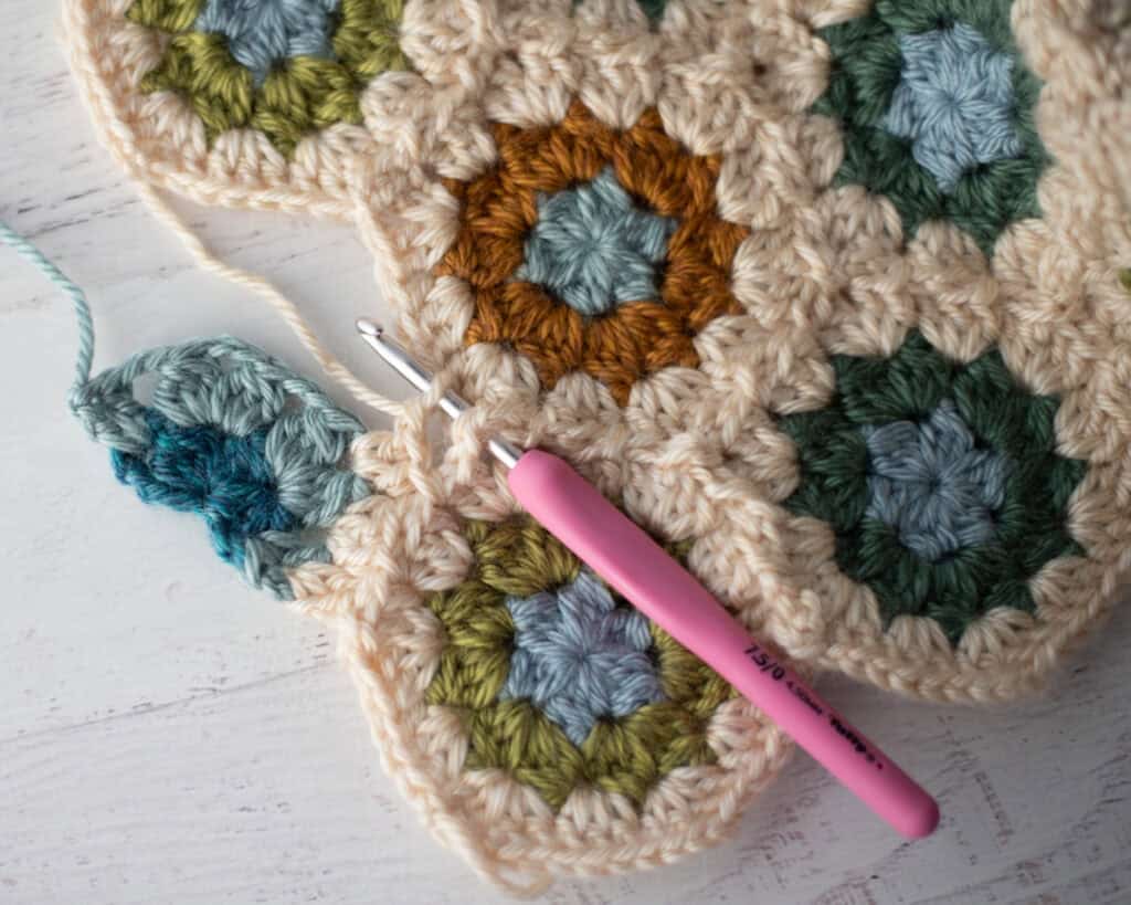 Close-up of crochet granny hexagons made with colorful yarn and a pink crochet hook.