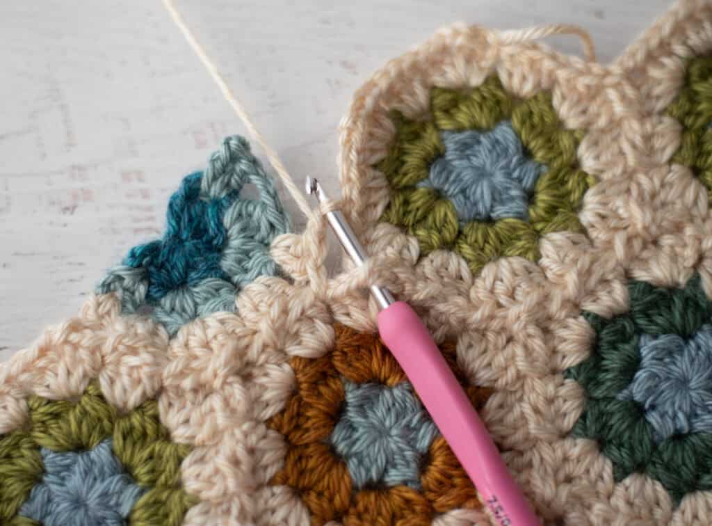 Close-up of crochet granny hexagons made with colorful yarn and a pink crochet hook.