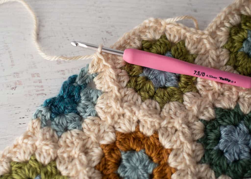 Close-up of crochet granny hexagons made with colorful yarn and a pink crochet hook.