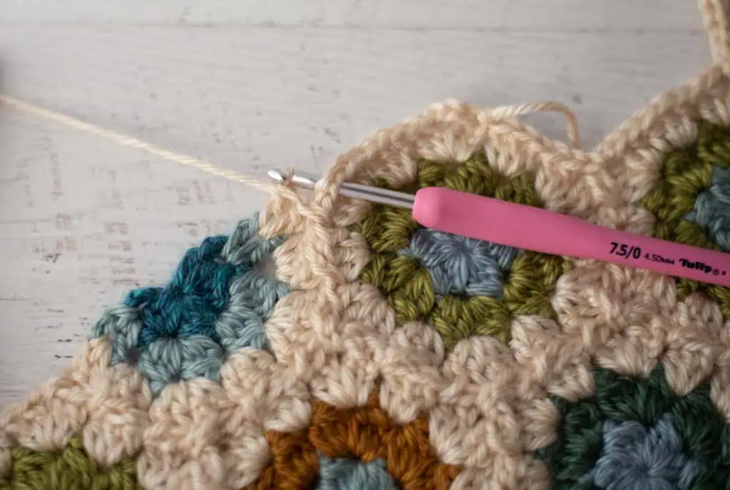 Close-up of crochet granny hexagons made with colorful yarn and a pink crochet hook.