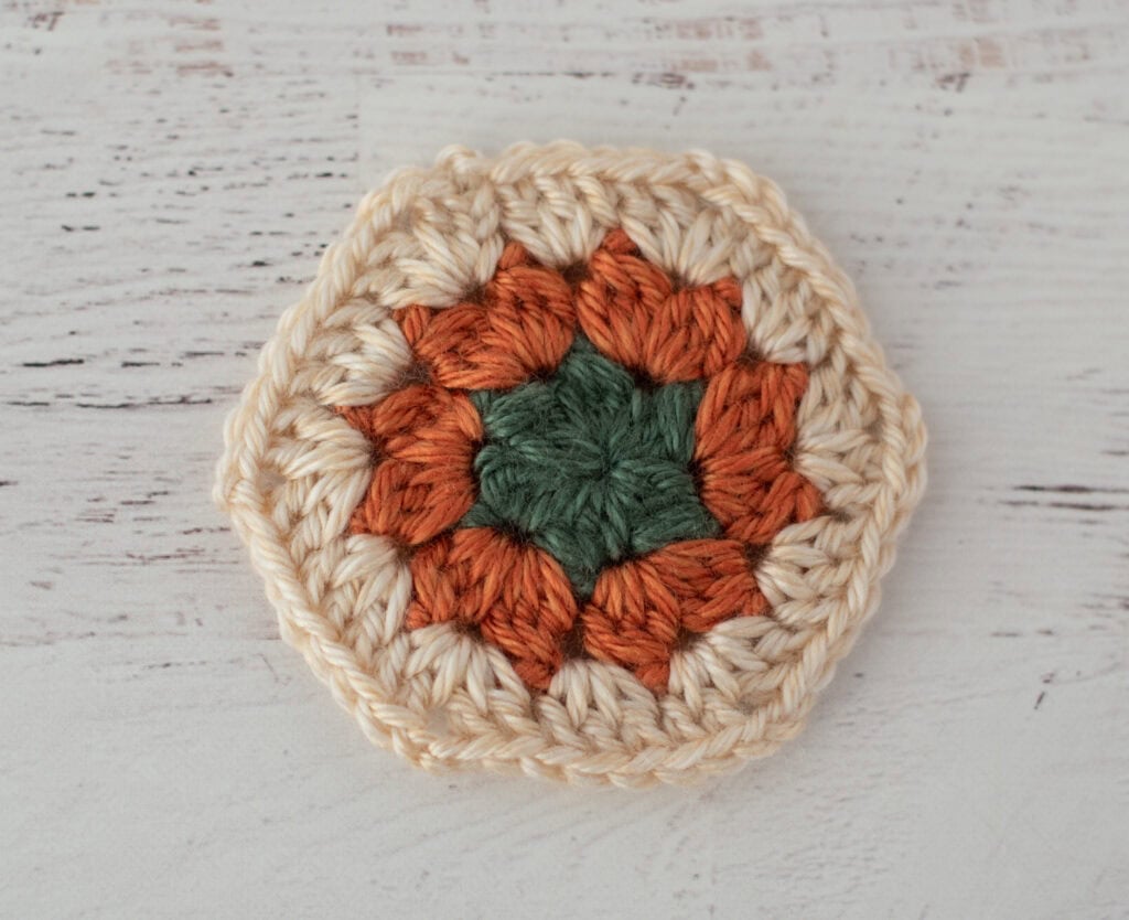 Crochet hexagon in green, orange and cream yarn.