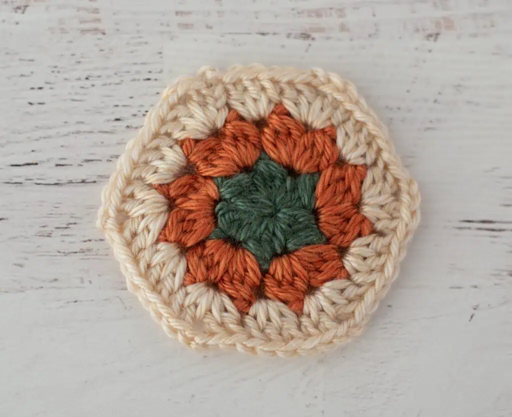 Crochet hexagon in green, orange and cream yarn.