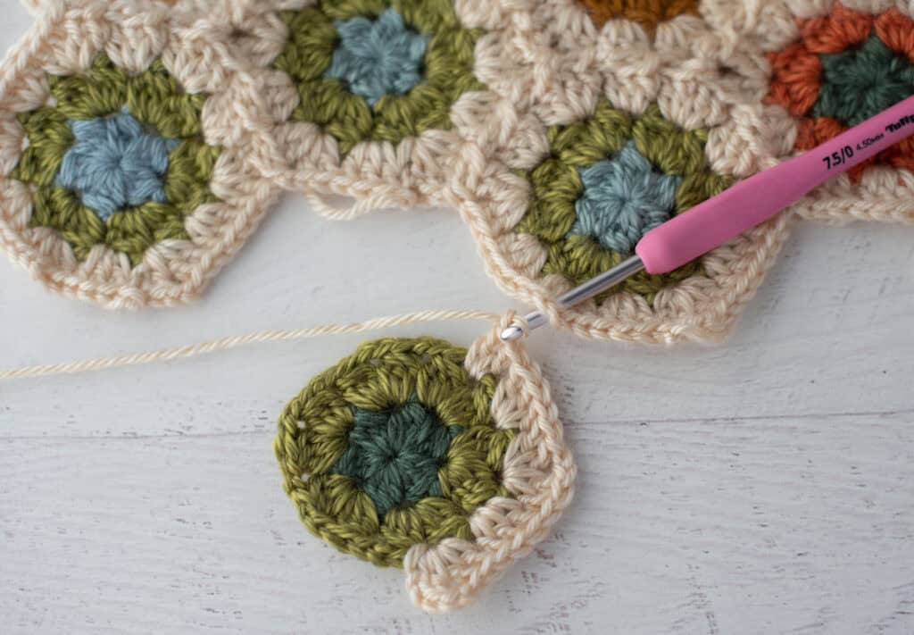 Close-up of crochet granny hexagons made with colorful yarn and a pink crochet hook.