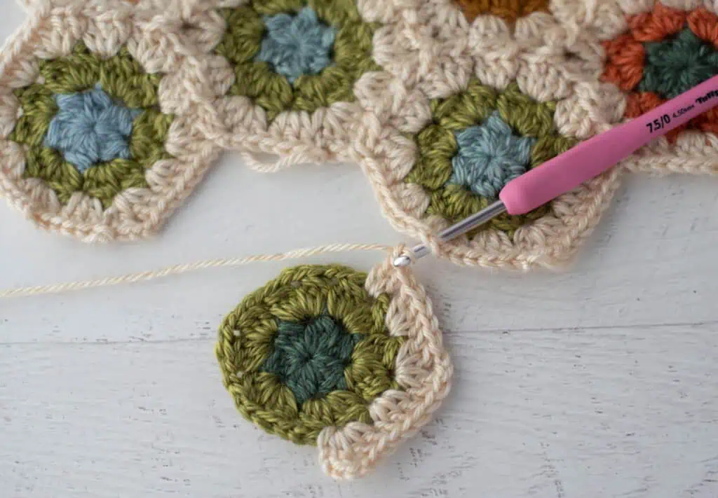 Close-up of crochet granny hexagons made with colorful yarn and a pink crochet hook.