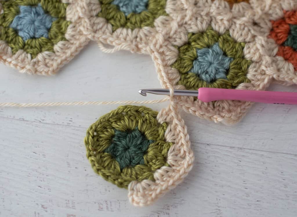 Close-up of crochet granny hexagons made with colorful yarn and a pink crochet hook.