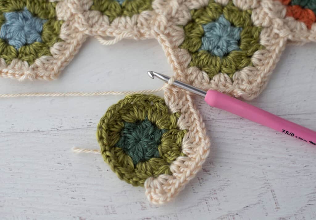 Close-up of crochet granny hexagons made with colorful yarn and a pink crochet hook.
