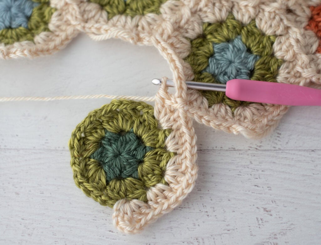 Close-up of crochet granny hexagons made with colorful yarn and a pink crochet hook.