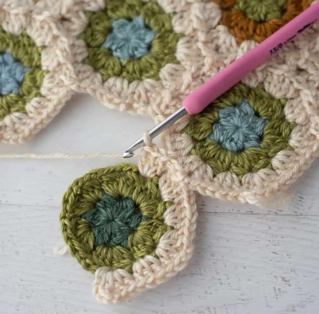 Close-up of crochet granny hexagons made with colorful yarn and a pink crochet hook.