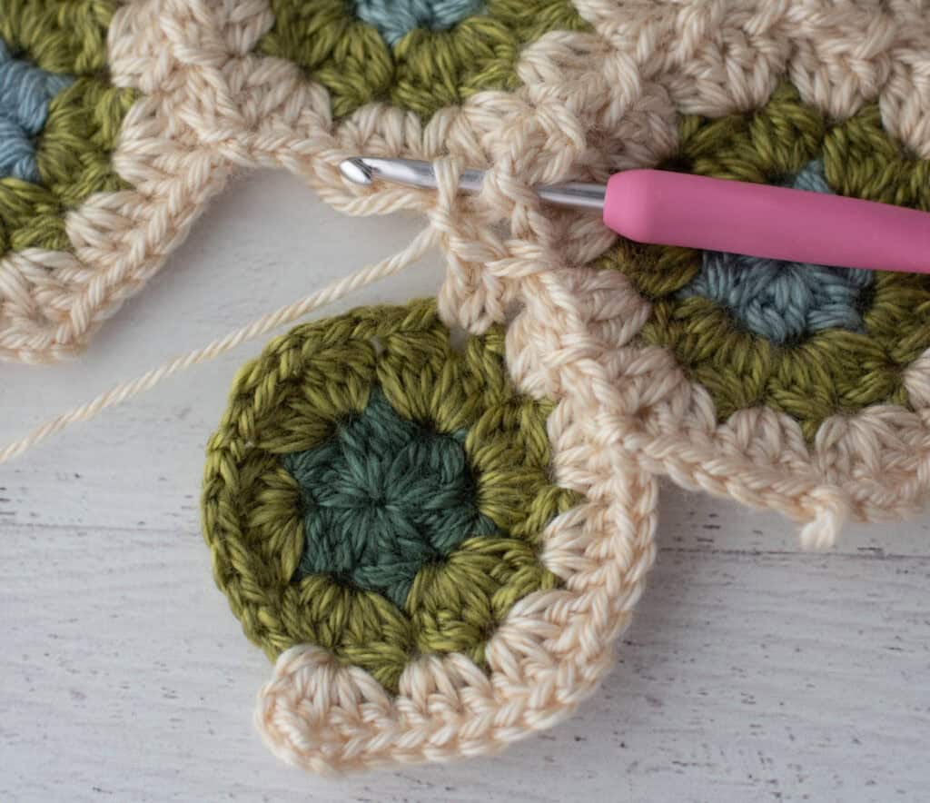 Close-up of crochet granny hexagons made with colorful yarn and a pink crochet hook.