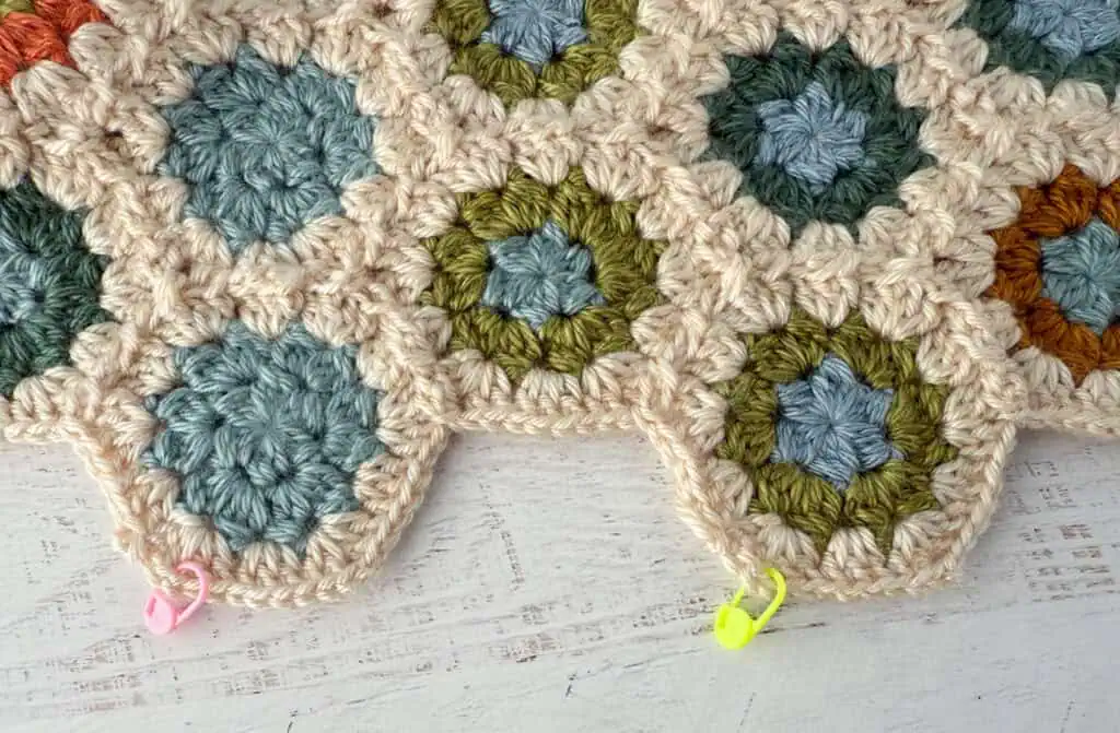 Close-up of crochet granny hexagon blanket bottom row in progress showing bright colored stitch markers