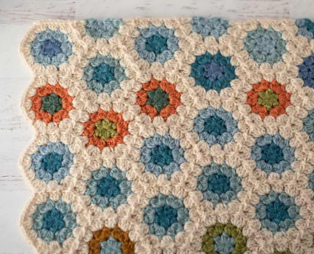 Corner of crochet granny hexagon blanket showing scallop side edge and straight top edge
