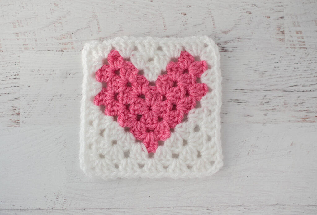 Pink crochet heart square on a white wooden surface
