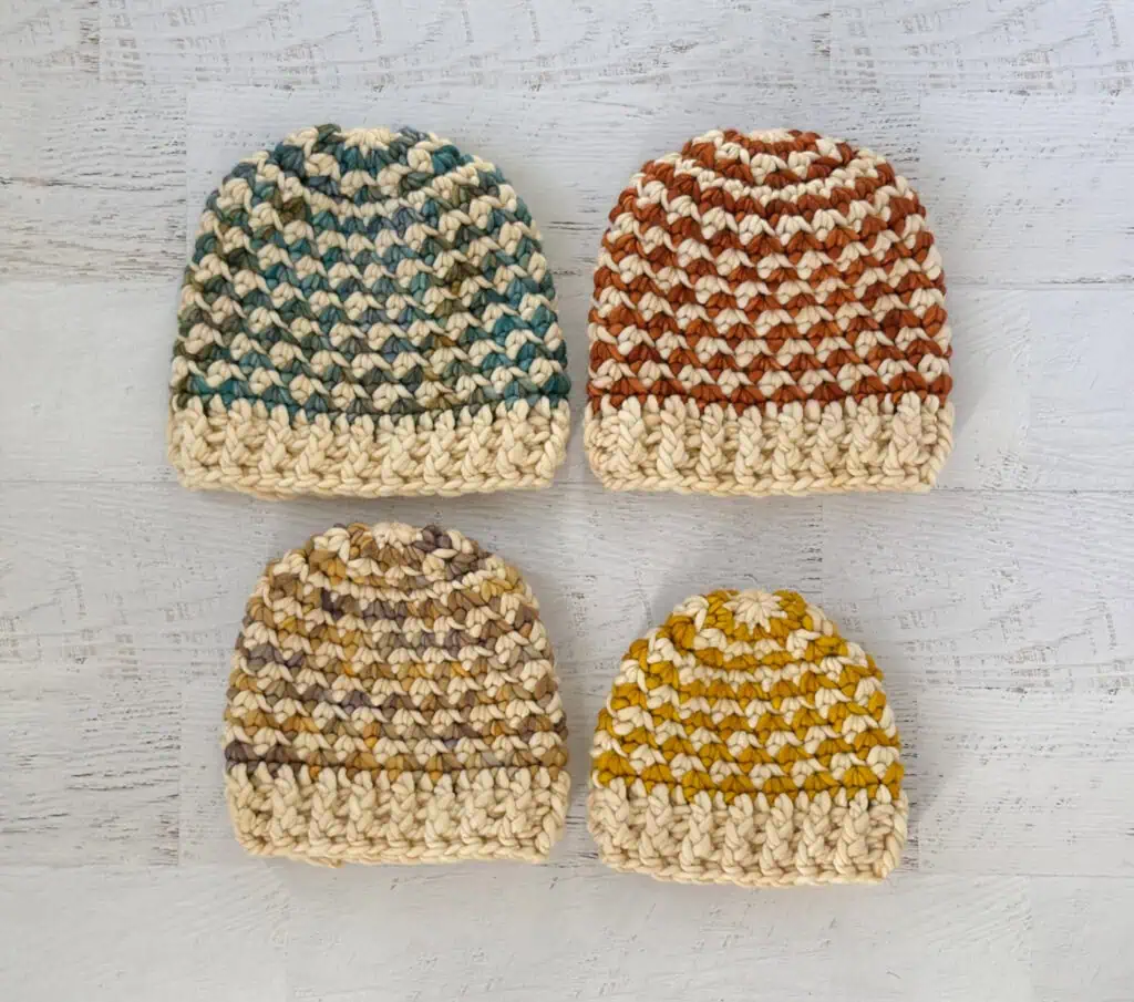 Colorful handmade crochet beanie hats on a whitewashed wood table