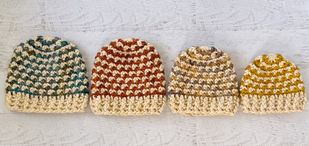 Colorful handmade crochet beanie hats on a whitewashed wood table