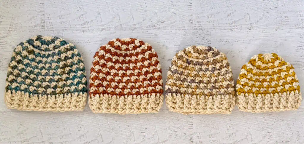 Colorful handmade crochet beanie hats on a whitewashed wood table