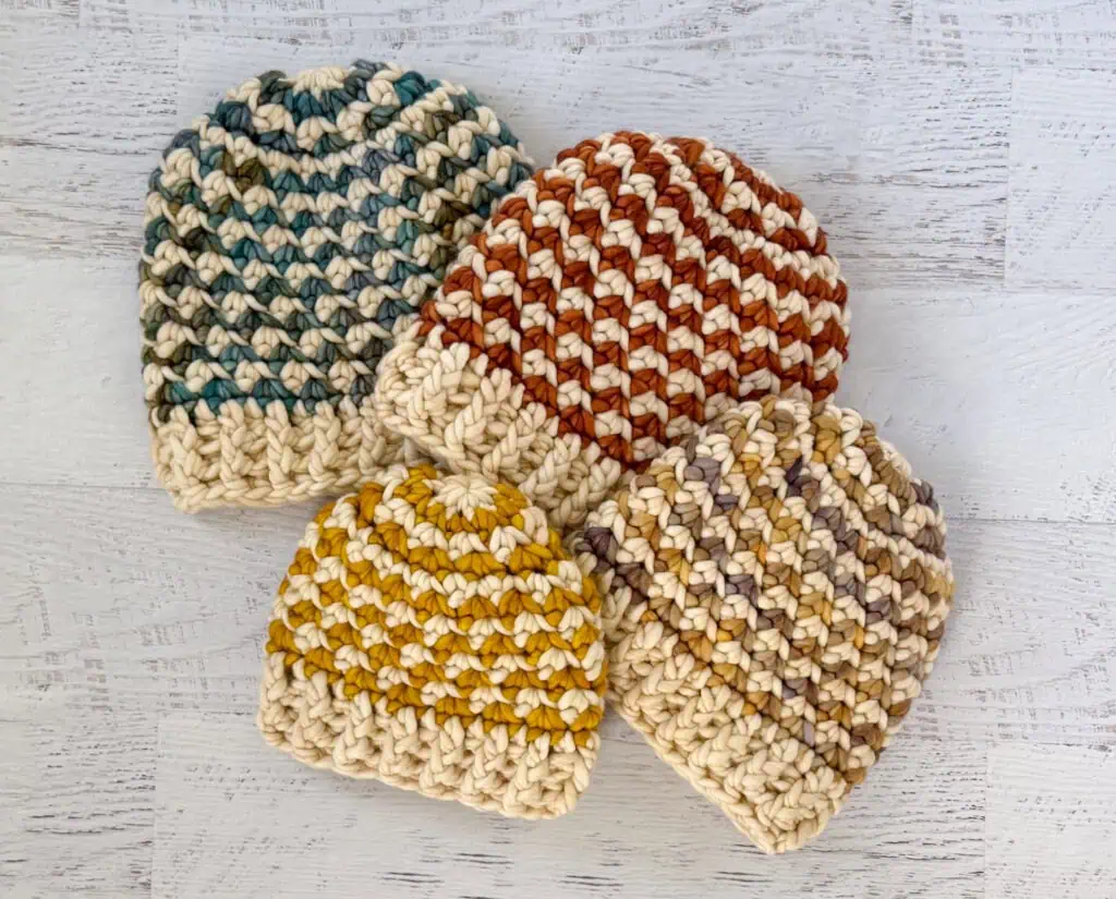 Colorful handmade crochet beanie hats on a whitewashed wood table