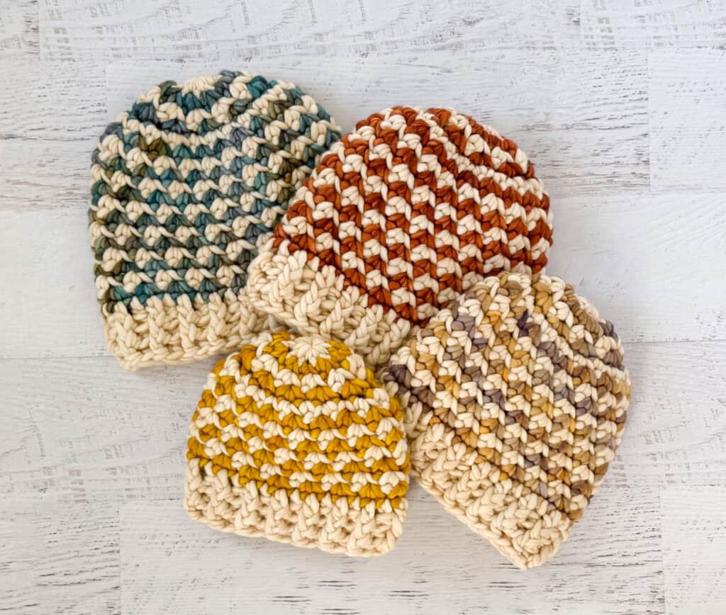 Colorful handmade crochet beanie hats on a whitewashed wood table