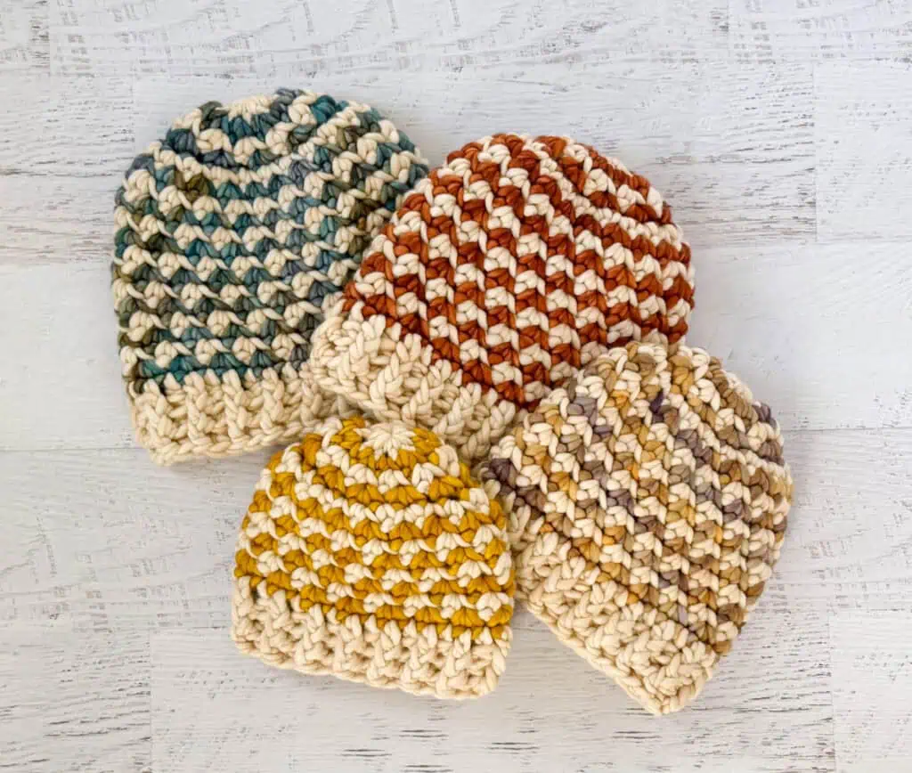 Colorful handmade crochet beanie hats on a whitewashed wood table