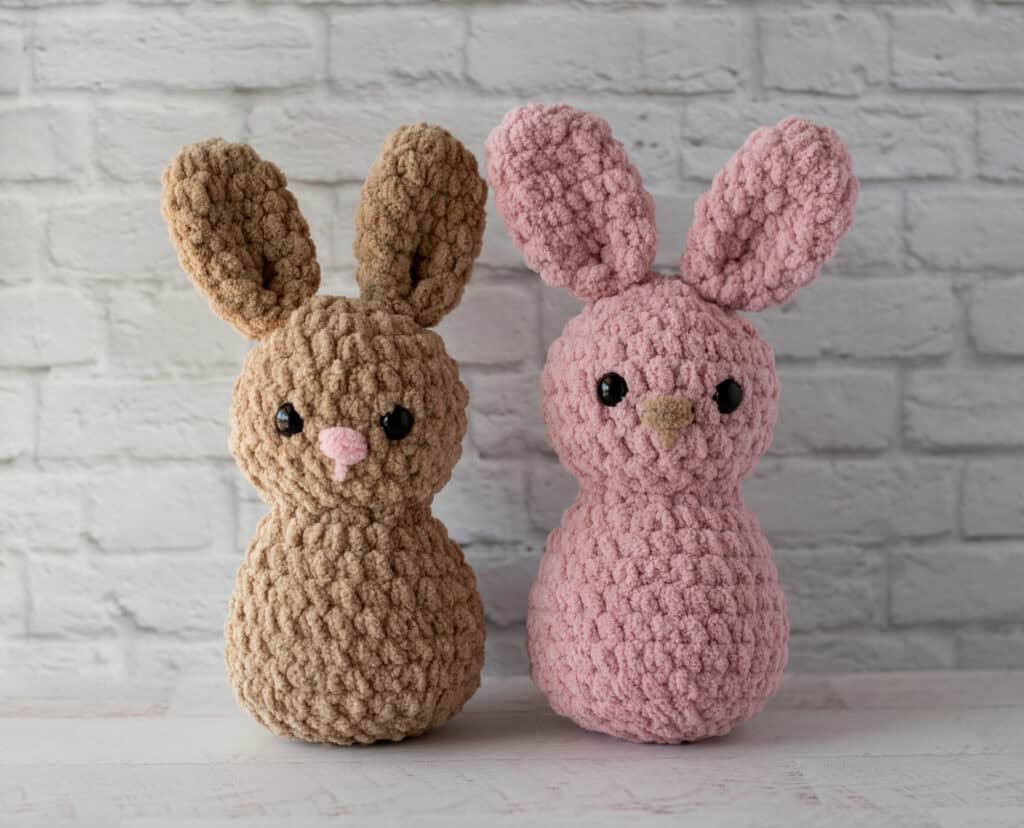 Two crochet bunnies. One is brown with a pink nose. The other is pink with a brown nose. Both have black eyes.