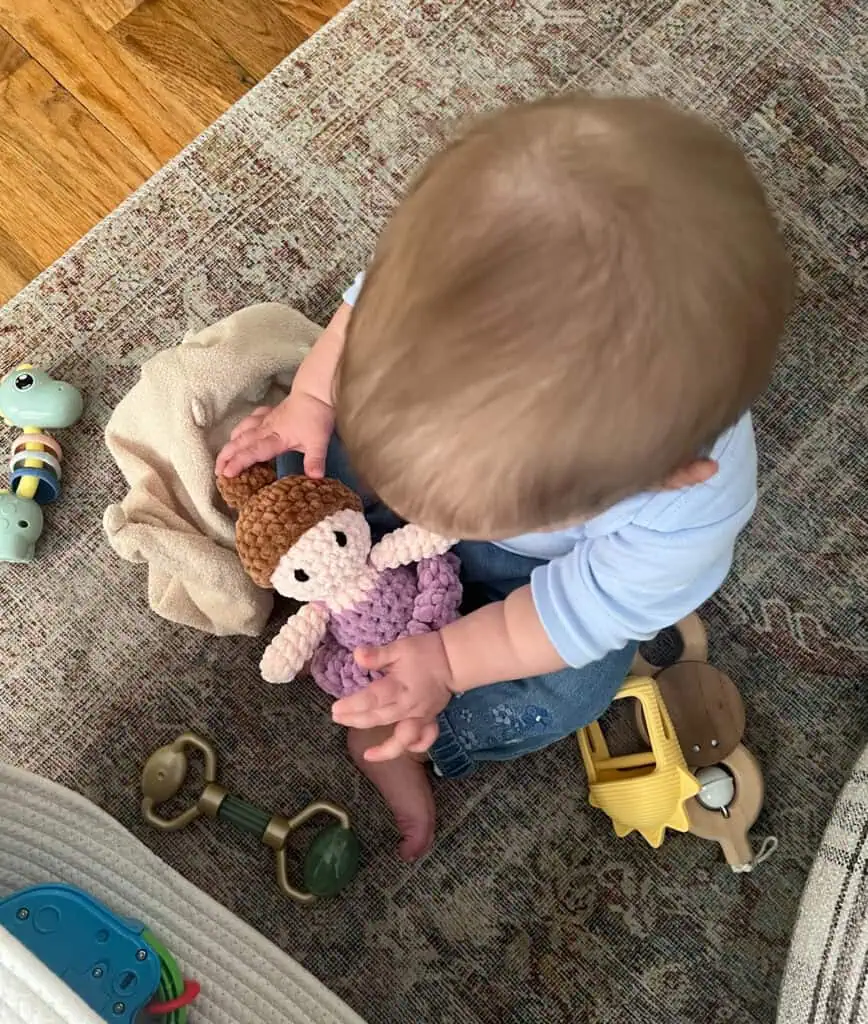 Baby on floor on rug with toys and crochet ballerina doll